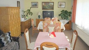 A dining area with a checkered tablecloth, wooden chairs, a television, and framed pictures on the wall. - App 2 (40m²) - Rügen-Fewo 267 (Mönchgut)