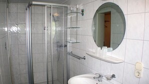 A bathroom with a glass shower enclosure, a white sink, a mirror, and a shelf with toiletries. - App 2 (40m²) - Rügen-Fewo 267 (Mönchgut)