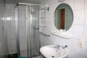 A bathroom with a glass shower enclosure, a white sink, a mirror, and a shelf with toiletries. - App 2 (40m²) - Rügen-Fewo 267 (Mönchgut)