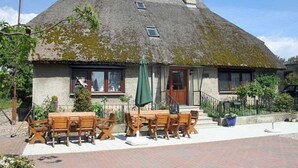A traditional stone house with a thatched roof, a wooden porch, and a brick patio with outdoor seating. - App 2 (40m²) - Rügen-Fewo 267 (Mönchgut)