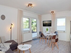 Un salon moderne avec un canapé, une table à manger et des chaises, un téléviseur fixé au mur et de grandes fenêtres.