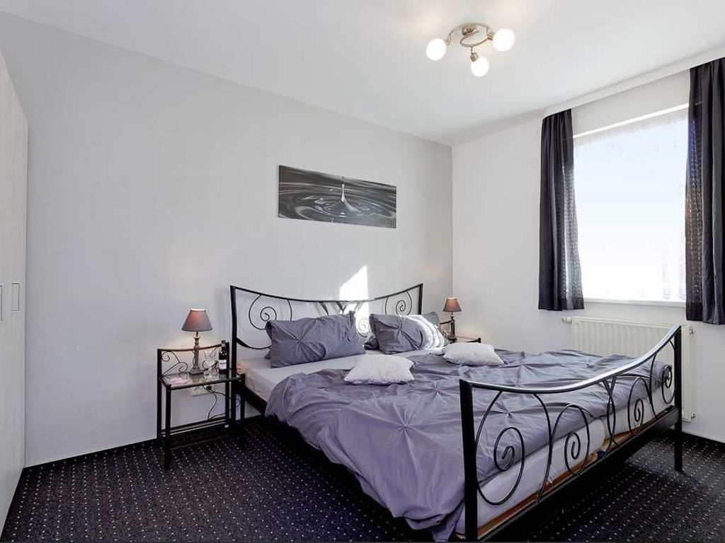 A bedroom with a bed, two bedside tables, a wall-mounted artwork, and a window with curtains.