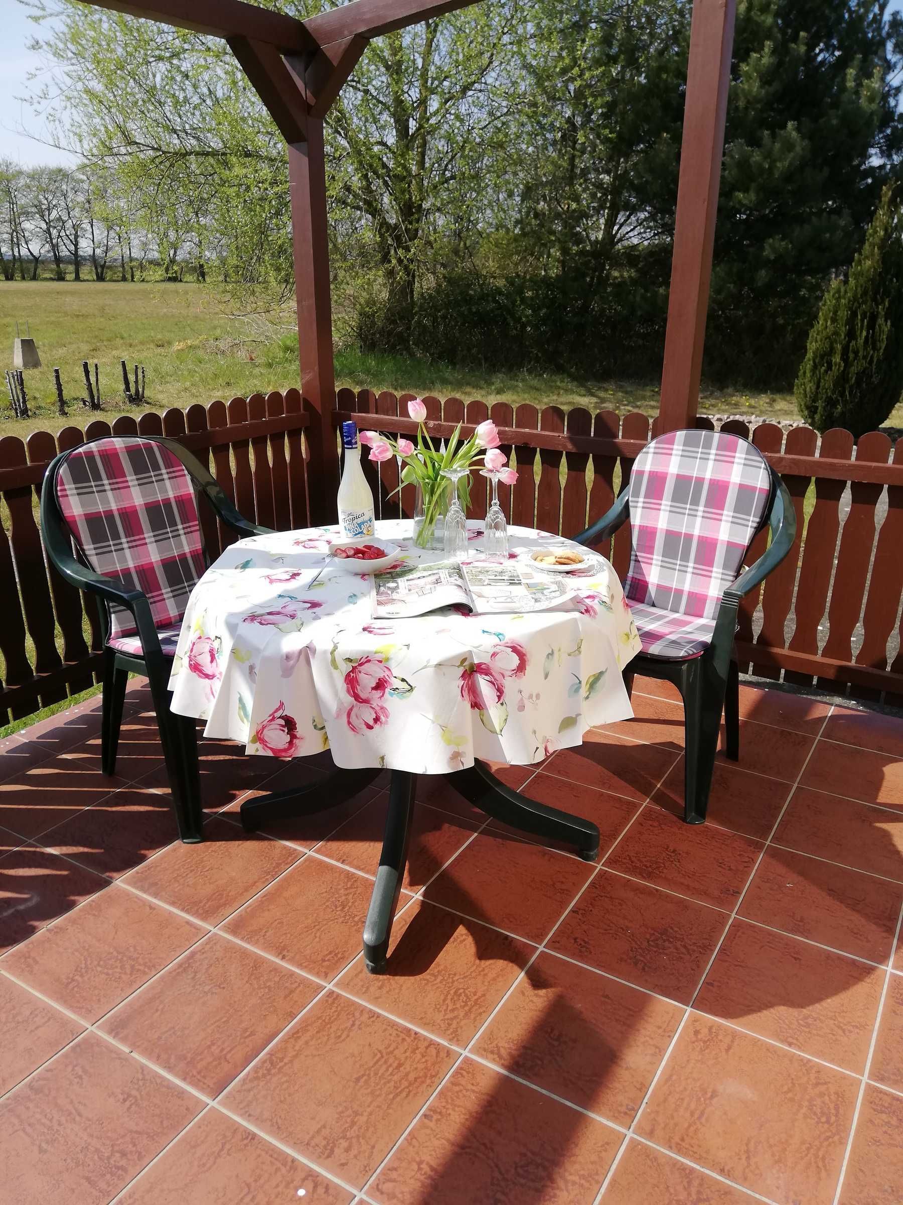 A patio with a table set for two, surrounded by a wooden fence, and chairs with floral upholstery.
