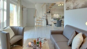 A modern living room with a sofa, a coffee table, and a dining area in the background.