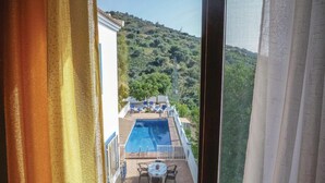 A pool area with a table and chairs, surrounded by a white railing and a view of a hillside.