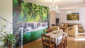 A dining area with a waterfall mural, a chandelier, and a sofa in a living room.