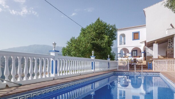 A swimming pool with a white balustrade, a patio area with outdoor seating, and a building with arched windows and a tiled roof.