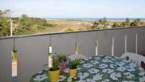 En balkon med et bord og stole, der kigger ud over en strand og åbne marker.