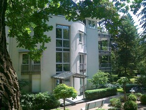 Un edificio de varios pisos con amplios ventanales, un balcón y un jardín bien cuidado.