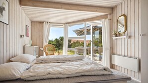 A bedroom with a large bed, a view of the outdoors, a wicker chair, and a mirror on the wall. - Amazing home in Blåvand with WiFi (Blåvand)