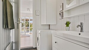 A modern kitchen with white cabinetry, a built-in washing machine, and a small sink with a plant. - Amazing home in Blåvand with WiFi (Blåvand)