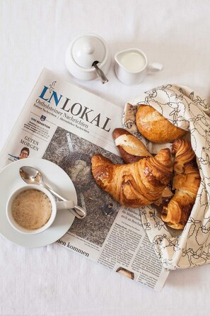 A breakfast setup with croissants, a cup of coffee, and a newspaper on a table.