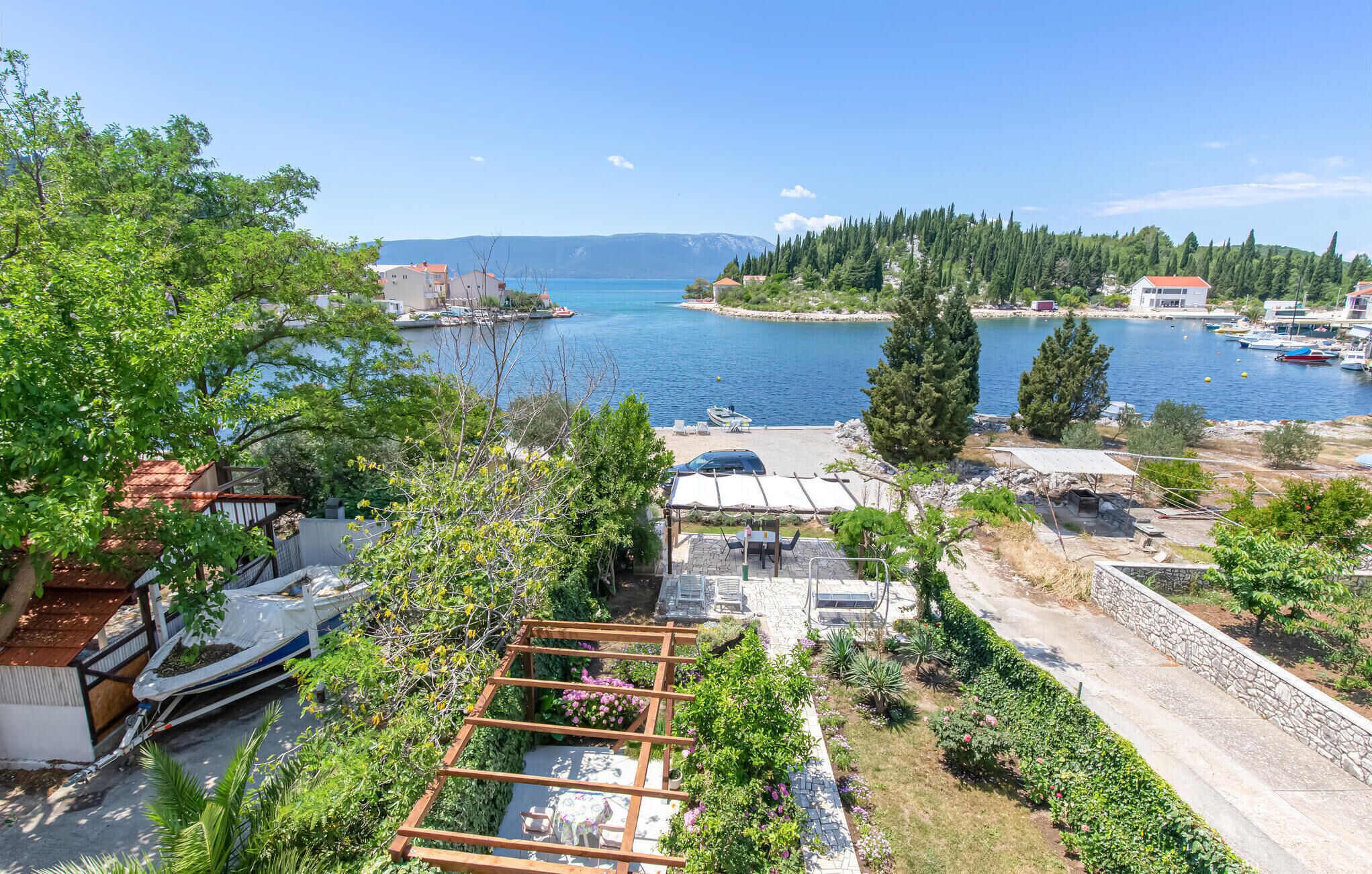Vista costera con cielo despejado, un puerto deportivo con barcos y una zona residencial con casas y vegetación.