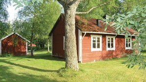 A red wooden house with white trim, surrounded by a well-maintained lawn and trees.