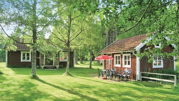 A rustic cabin with a red roof and white trim, surrounded by lush greenery and trees.