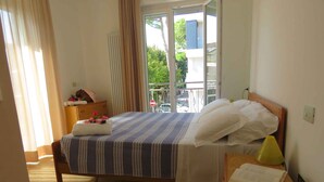 A hotel room with a bed, a bedside table with a lamp, a window with a view of the outside, and a door. - Holiday apartment with balcony in close proximity to the beach (Riccione)
