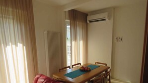 A dining area with a table, chairs, and a fruit bowl. There is an air conditioning unit on the wall. - Holiday apartment with balcony in close proximity to the beach (Riccione)