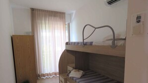 A bunk bed room with a wooden wardrobe, a small bedside table, and a window with curtains. - Holiday apartment with balcony in close proximity to the beach (Riccione)