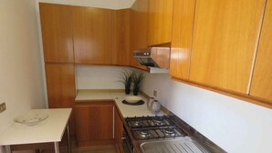 A compact kitchen with wooden cabinets, a gas stove, and a small countertop. - Holiday apartment with balcony in close proximity to the beach (Riccione)
