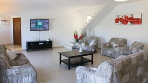 Un salon comprenant un téléviseur, une table basse, deux fauteuils à motifs, un canapé et un escalier.
