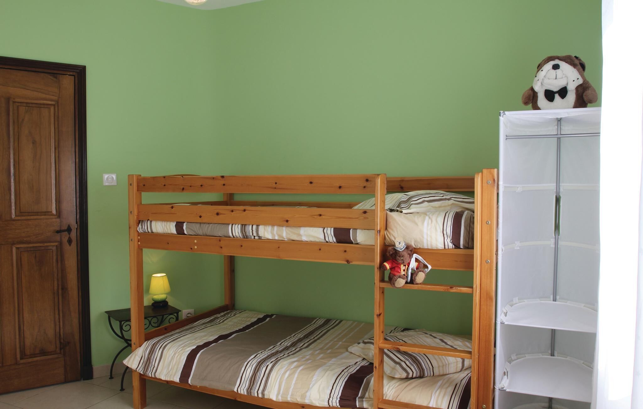 A bunk bed with striped bedding, a small table with a lamp, and a teddy bear on the top bunk.