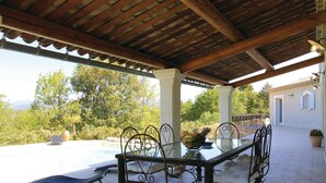 Une terrasse extérieure avec une piscine, une table et des chaises, et une vue sur les arbres et les montagnes.