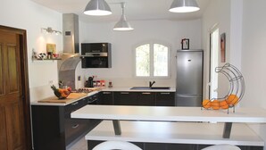Une cuisine moderne dotée d’un îlot central, de meubles de couleur noire, d’appareils électroménagers en acier inoxydable et de luminaires suspendus.