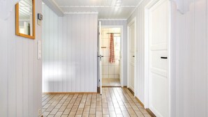 Un couloir aux murs recouverts de panneaux blancs, doté d’un sol carrelé et d’une porte donnant sur une salle de bain avec un rideau de douche.