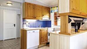 Une cuisine avec des meubles en bois, un lave-vaisselle blanc, un crédence en carrelage bleu et une fenêtre agrémentée d’un rideau coloré.