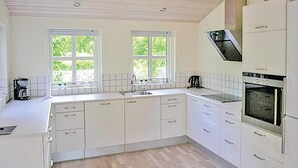 A kitchen with white cabinets, a built-in oven, and two windows with a view of greenery. - Amazing home in Glesborg with sauna (Glesborg)