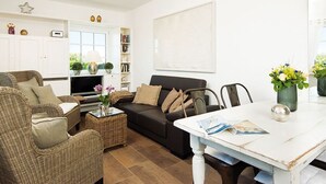Un salon comprenant un canapé, des fauteuils, une table basse et un téléviseur. On y trouve également une bibliothèque remplie de livres et d’objets décoratifs.