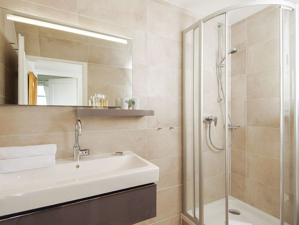 Un baño moderno con lavamanos blanco, espejo y cabina de ducha con paredes de vidrio.