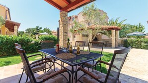 Un patio al aire libre con una mesa y sillas, rodeado de pilares de piedra y follaje.
