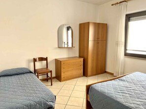 Une chambre avec deux lits, une armoire en bois, une chaise, une commode et un miroir.