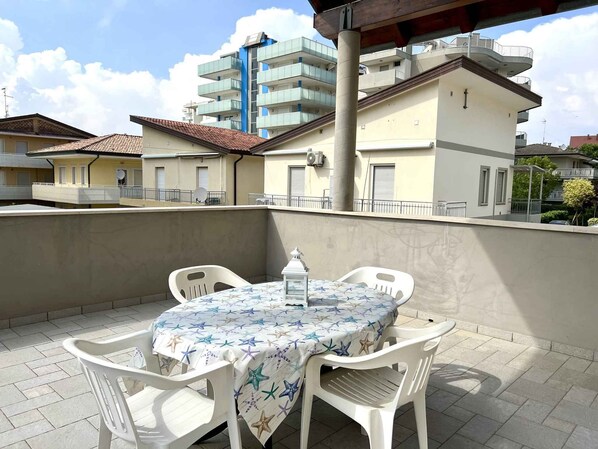 Une terrasse avec une table et des chaises, une lanterne blanche et une vue sur des immeubles d’habitation.