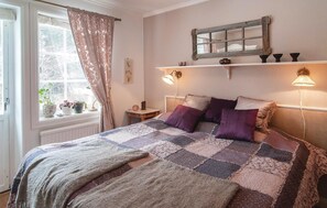 Ein gemütliches Schlafzimmer mit einem großen Bett, zwei Nachttischlampen, einem Fenster mit Vorhängen und einer Ablage mit Dekoration.