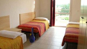 A hotel room with two single beds, a small table, and a window with a view of greenery. - Holiday apartment with pool and air conditioning (Peschiera del Garda)