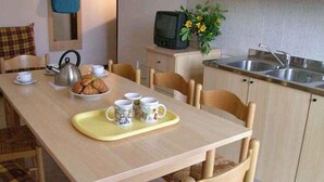 A small, cozy kitchen with a dining table set for two, a kettle, a plate of croissants, and a tray with two mugs. - Holiday apartment with pool and air conditioning (Peschiera del Garda)