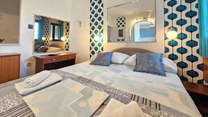 Habitación de hotel con una cama grande, una mesita de noche, un espejo y un papel tapiz estampado.