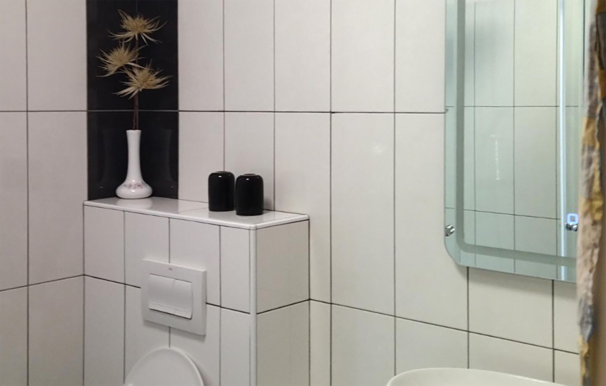 A bathroom with white tiles, a toilet, a white sink, and a black vase with dried plants.