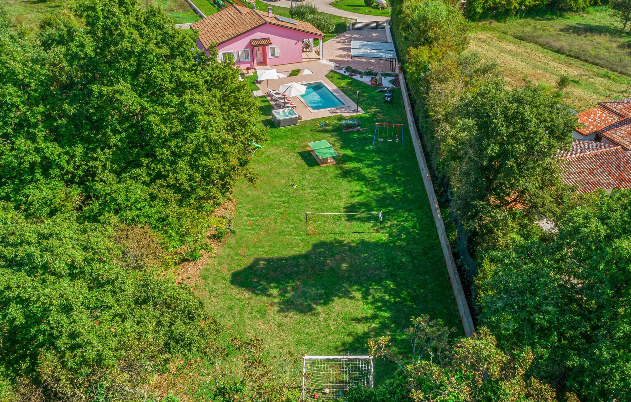 An aerial view of a residential area with a pink house, a swimming pool, and a tennis court.