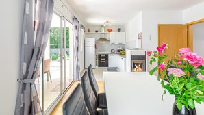 Eine moderne Küche mit Kamin, einem Essbereich mit Tisch und Stühlen sowie Blick auf den Garten durch die Schiebetür.