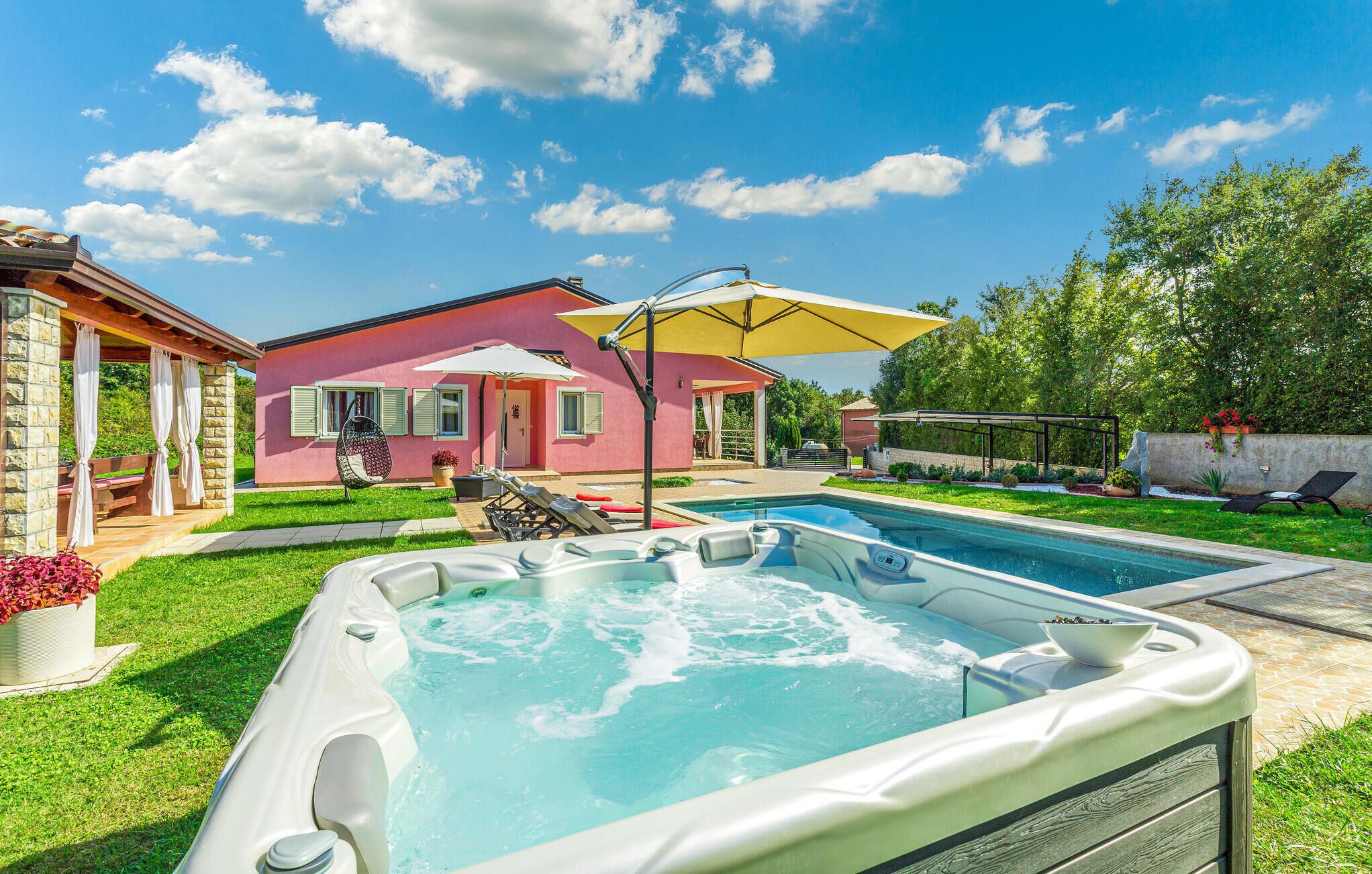 Ein Garten mit Swimmingpool, Whirlpools, einer überdachten Terrasse und einem rosafarbenen Haus.