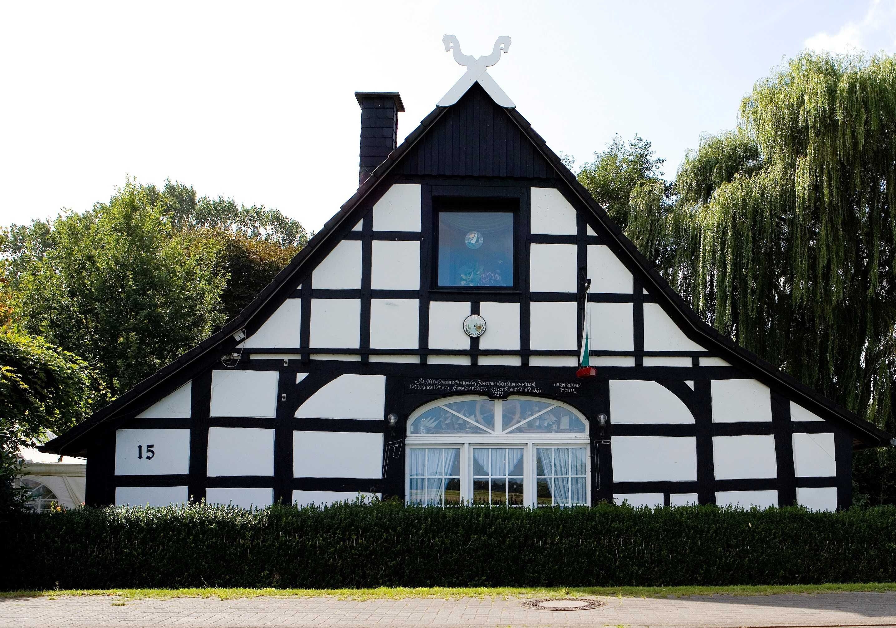 A traditional half-timbered building with a black and white facade, a chimney, and a window with curtains.