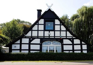 Un bâtiment traditionnel à colombages, avec une façade noire et blanche, une cheminée et une fenêtre ornée de rideaux.