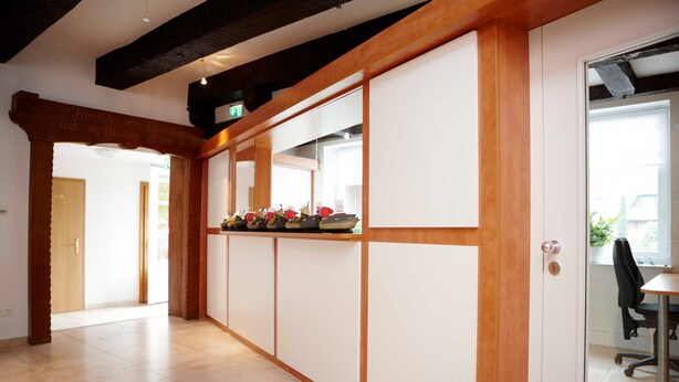 Un pasillo con un banco de madera, una puerta y vistas a una habitación con una mesa y una silla.