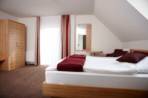 Una habitación de hotel con cama, armario, espejo y ventana con cortinas.