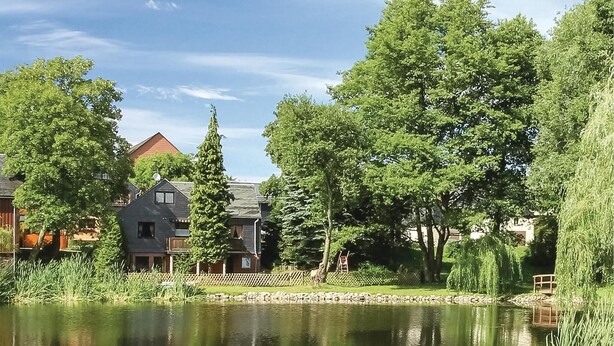 Eine friedliche Uferlandschaft mit einem Haus, einem hölzernen Steg und üppigem Grün.