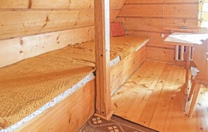 Eine Holzhütte mit einem Schlafplatz auf Schrankbett, einem kleinen Tisch und einem Fenster mit Vorhang.