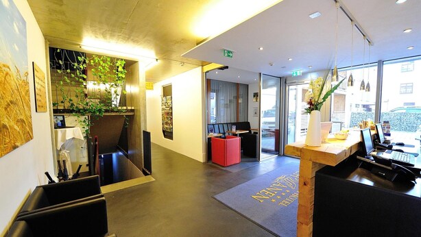 Un hall d’hôtel moderne doté d’un comptoir d’accueil, d’un espace salon et d’une grande fenêtre donnant sur la rue.
